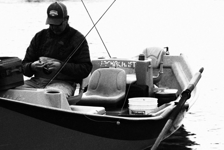 Man sitting in a fishing boat looking down and wearing an Orvis hat